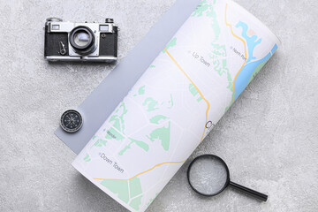 Photo camera, compass, magnifying glass and rolled map on grey background