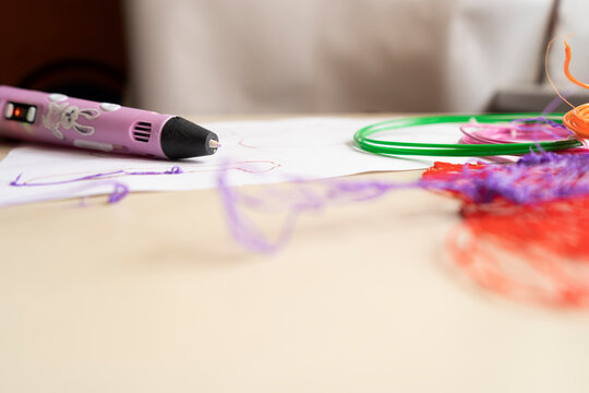 Toys made of plastic wire. Multicolored coils of wire on the table. The child makes figures with a pink 3-d pen.