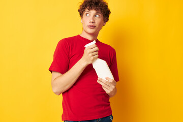 cute red-haired guy in a red t-shirt detergents in hands posing yellow background unaltered