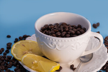 Coffee beans in a white mug on a saucer. There are lemon slices on a plate.