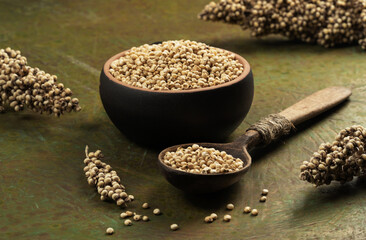 White sorghum seeds in a wooden bowl with a spoon on a green background.