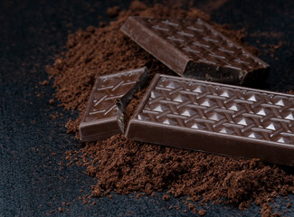 Bars of black tasty chocolate on a dark background. Calorie food.
