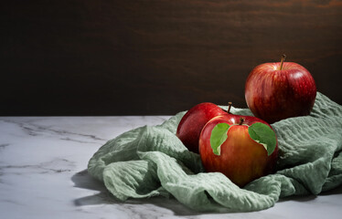 red apples with green leaves on a marble table on a burlap napkin, low key