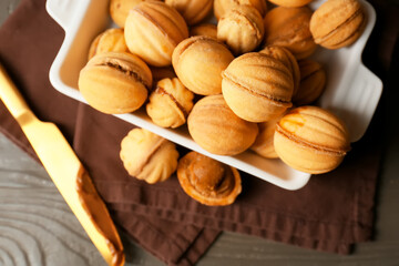 Baking dish of tasty walnut shaped cookies with boiled condensed milk on dark wooden background, closeup