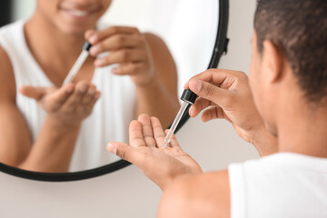 Young African-American guy using serum for skin care in bathroom