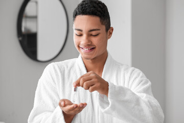 Young African-American guy using serum for skin care in bathroom