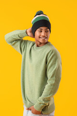 Handsome African-American guy in knitted sweater on yellow background