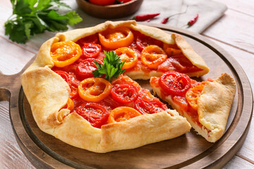 Board with tasty tomato galette on light wooden background, closeup