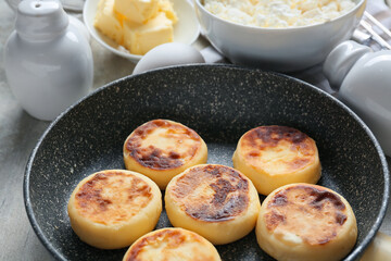 Frying pan with tasty cottage cheese pancakes on table, closeup