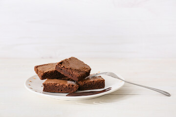 Plate with pieces of tasty chocolate brownie on white wooden background