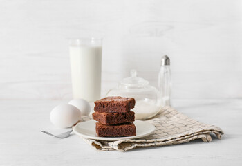 Plate with pieces of tasty chocolate brownie on white wooden background