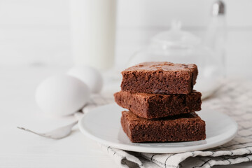 Plate with pieces of tasty chocolate brownie on white wooden background