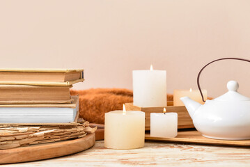Fototapeta na wymiar Stack of books with burning candles and teapot on light wooden table