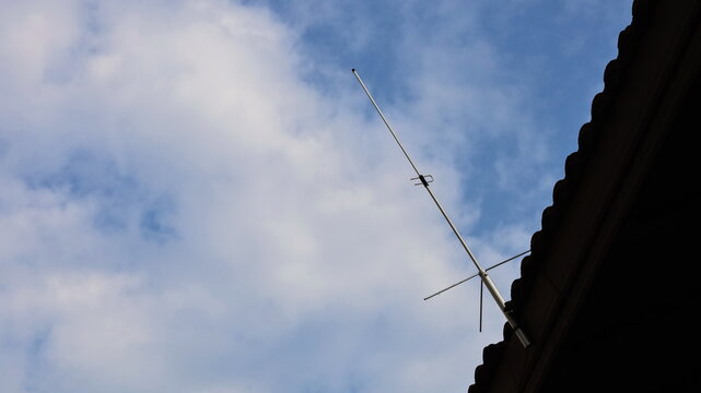 Communication antenna on the roof. Single Side Band (SSB) high frequency radio transmitting metal antenna on roof of house with blue sky background with white clouds with copy space. Selective focus