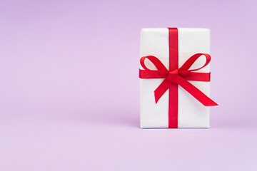 Valentine's Day or birthday concept with copy space. White gift box with red ribbon on purple papper