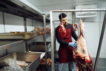Male butcher standing by meat hanging on hook in meat shop