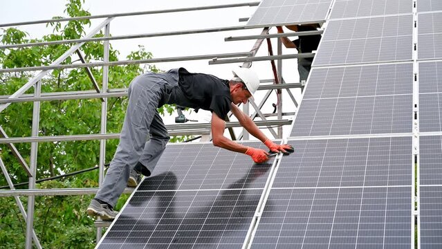 Workers mounting photovoltaic solar panel system outdoors. Men engineers placing solar module on metal rails, wearing construction helmets and work gloves. Renewable and ecological energy.