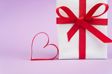 Valentine's Day or birthday concept with copy space. Red ribbon heart and gift box on purple papper
