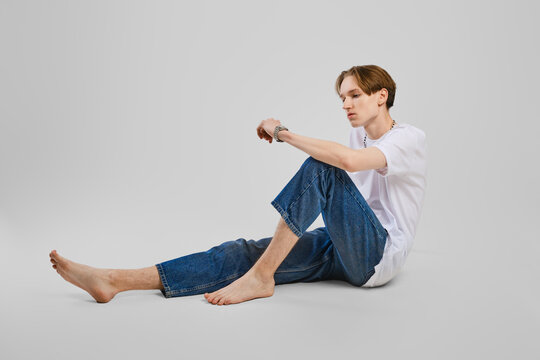 Young barefoot man sits on the floor in studio in white t-shirt and jean