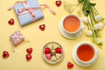 Composition with tasty heart-shaped candies, flowers and cups of tea for Valentine's Day celebration on beige background