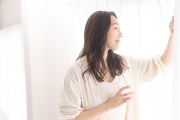 水の入ったグラスを持ちカーテンを開ける女性