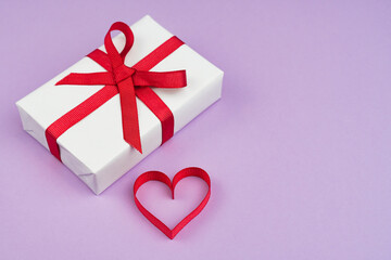 Valentine's Day or birthday concept with copy space. Red ribbon heart and gift box on purple papper