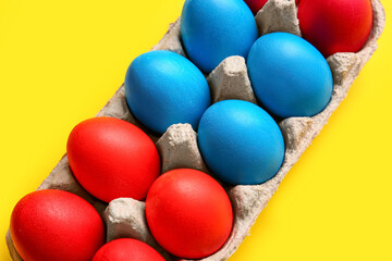 Fototapeta na wymiar Holder with red and blue Easter eggs on color background