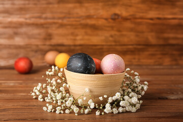 Bowl with multicolored Easter eggs and gypsophila flowers on wooden background