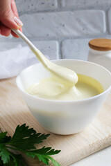 A woman's hand holds a teaspoon of mayonnaise over a white bowl with sauce. The concept of proper nutrition. Vertical orientation.