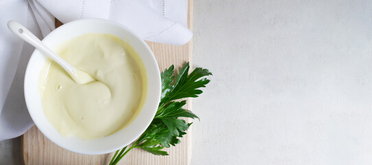 Homemade mayonnaise in a white bowl on a wooden cutting board with a sprig of parsley. The concept of proper nutrition. Horizontal orientation. Banner. copy space.