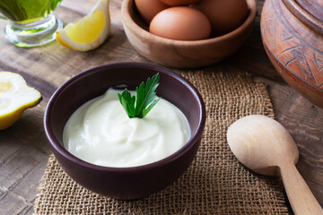 Homemade mayonnaise in a brown bowl with ingredients in the background on a wooden table. The concept of proper nutrition. Rustic. Horizontal orientation.