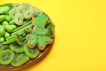 Wooden board with different sweets for St. Patrick's Day celebration on yellow background, closeup