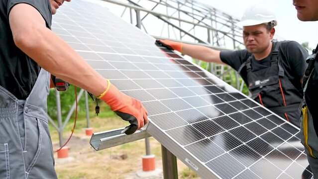 Workers installing solar panel on metal beams. Close up image of men wearing workwear and helmets
