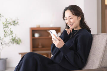 リビングのソファー座り携帯電話を見ている日本人女性