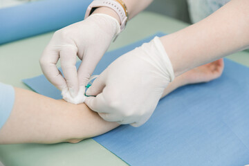 Taking a blood test from a vein in the treatment room. Nurse pricking a syringe with a needle into the patient hand. Swab pressed against the injection site during blood donation. Tube with blood.