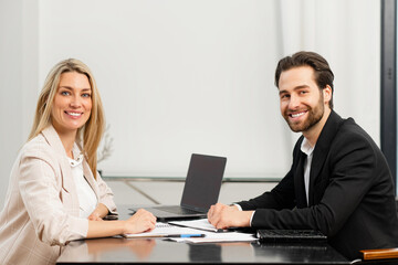 Obraz premium Young caucasian coworkers working out business strategy together and discuss tasks while sitting at the office desk and looking at the camera. Team work concept