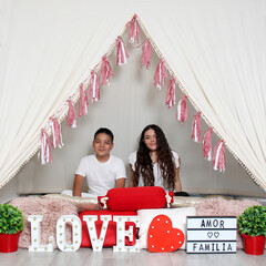 Hispanic brother and sister show love under a teepee with a sign that says 