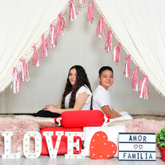 Hispanic brother and sister show love under a teepee with a sign that says 