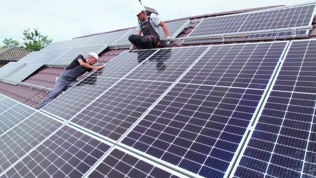 Men workers installing photovoltaic solar moduls on roof of house. Engineers in helmet building solar panel system outdoors. Concept of alternative and renewable energy. Aerial view.