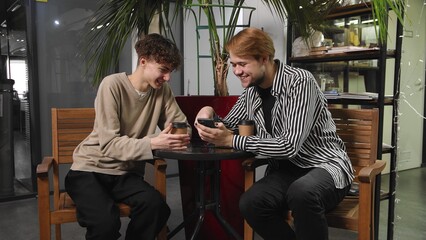 Two gay guys on a date are sitting in a cafe, drinking coffee and looking at photos on their phone. LGBT