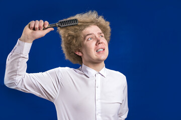 Comb curly hair. Pain. A curly-haired man in a shirt winces in pain as he brushes his hair. Salon. Humor. Suffering