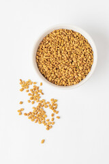 Scattered yellow fenugreek seeds or shambhala, helba seeds  on white background, top view. Fenugreek is ingredient of traditional Indian cuisine