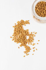 Scattered yellow fenugreek seeds or shambhala, helba seeds  on white background, top view