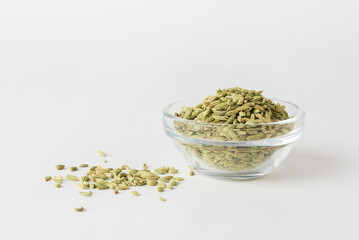 Scattered green dry fennel seeds on white background. fennel is ingredient of traditional Indian cuisine in the glass bowl