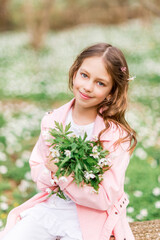 Fototapeta premium Portrait of a girl with a bouquet of anemone. A child in the spring forest.
