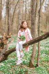 Portrait of a girl with a bouquet of anemone. A child in the spring forest.