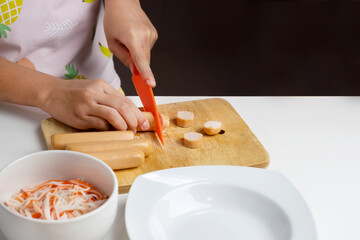 The hands of an Asian girl and his mother are cutting sausages to prepare a dinner menu.