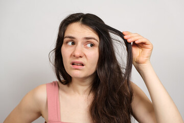 Fototapeta premium A beautiful brunette woman without makeup with dirty oily hair holds her hands on her head with a dissatisfied look