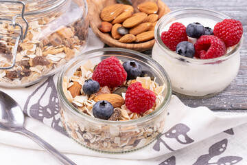 Close-up of granola with nuts, raspberries and blueberries, yogurt on a gray whitewashed rustic table, copy space. healthy breakfast