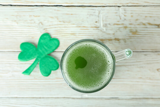 Glass of ale and clover leaf on white wooden table